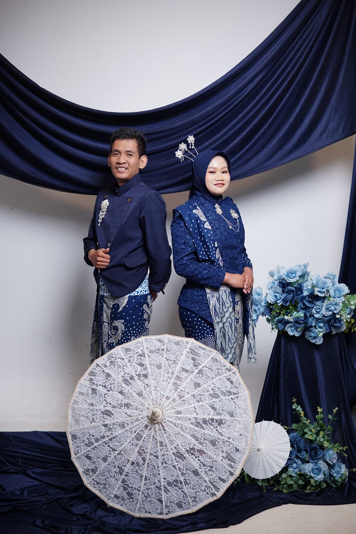 Ula dan Fadli berdiri berdampingan dalam busana biru bernuansa tradisional